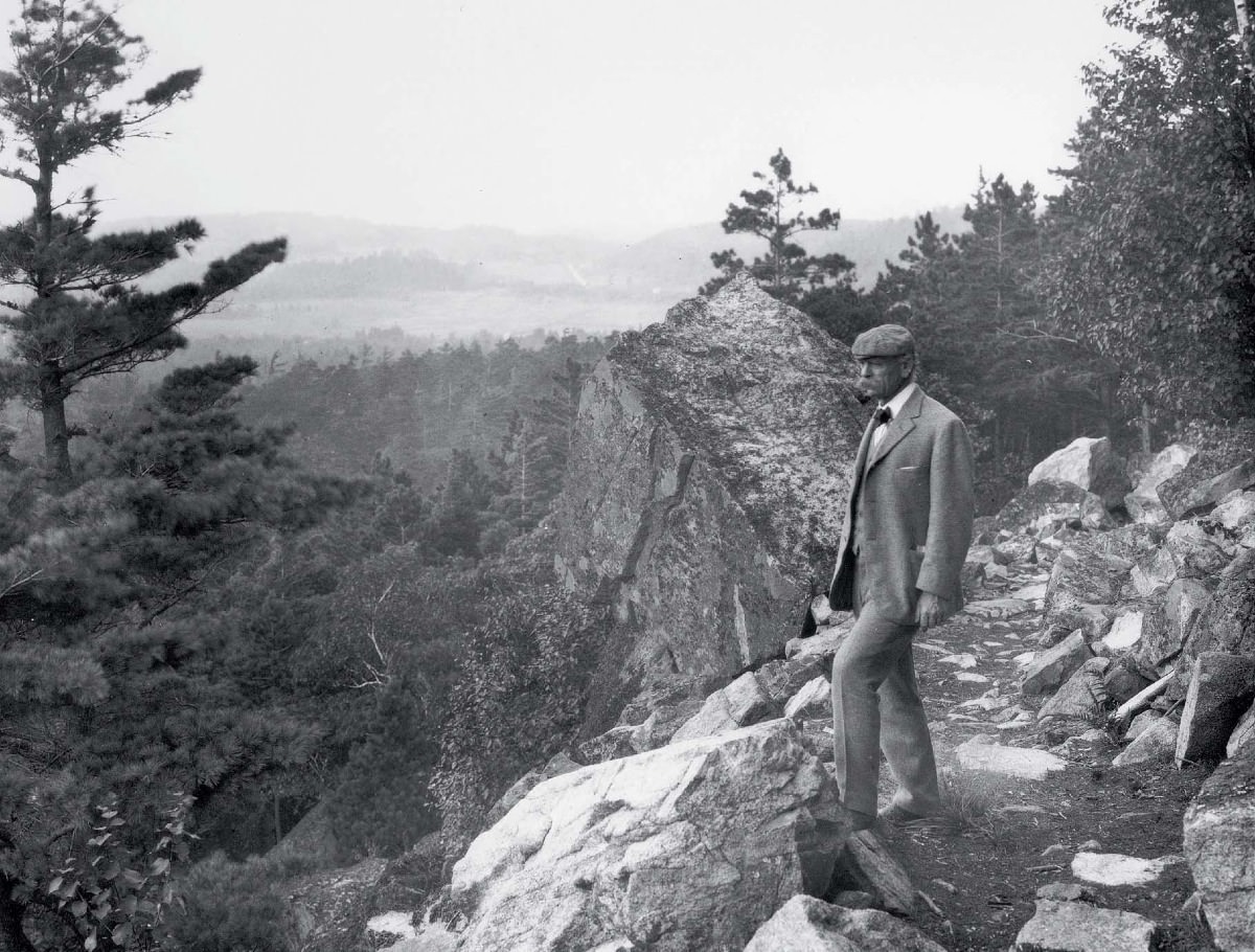 A black and white photo of George B. Dorr standing on a cliff, overlooking Acadia.