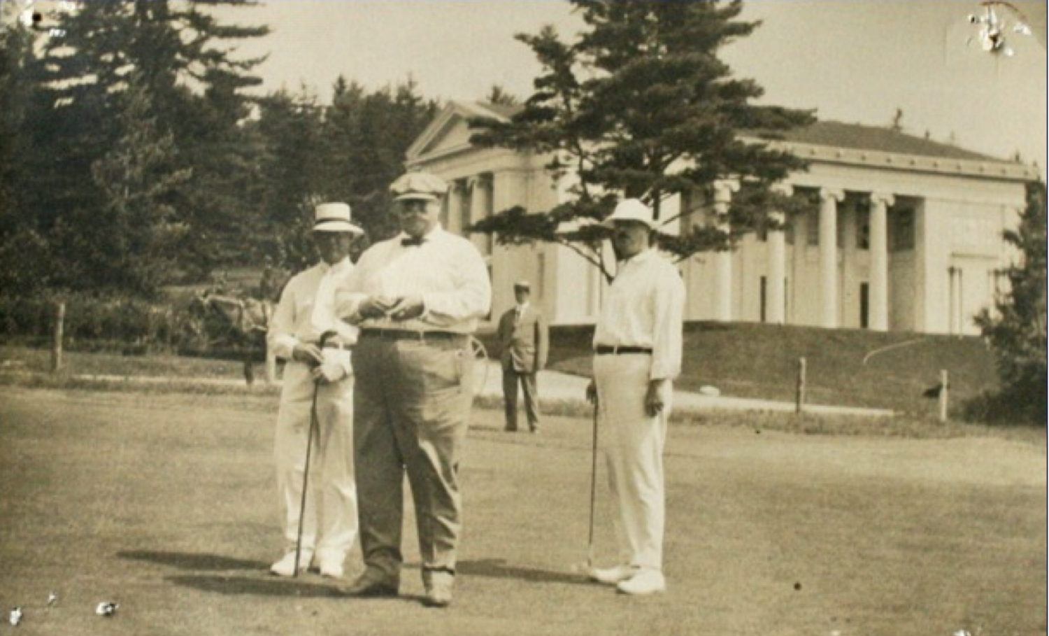 A photo of President Taft at Kebo Golf Club, standing on the green in front of the Building of Arts. 